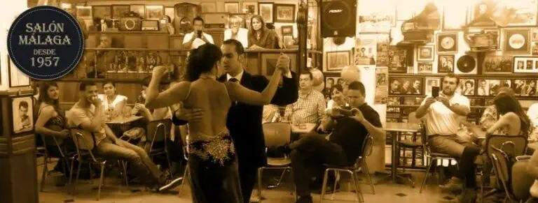 Couple dansant le tango dans une salle de bal avec des participants qui regardent, décor vintage et atmosphère chaleureuse lors d'un événement culturel à Medellín.