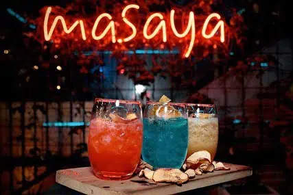 色彩缤纷的软饮料盛在装满冰块的玻璃杯中，气氛欢快，霓虹灯招牌上写着“masaya”。