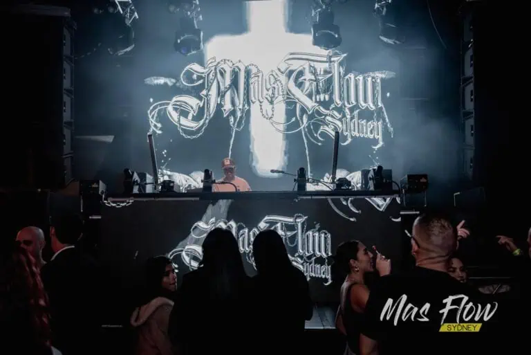 DJ en vivo en evento musical con pantalla LED grande mostrando "Mas Flow Sydney" en un concierto.