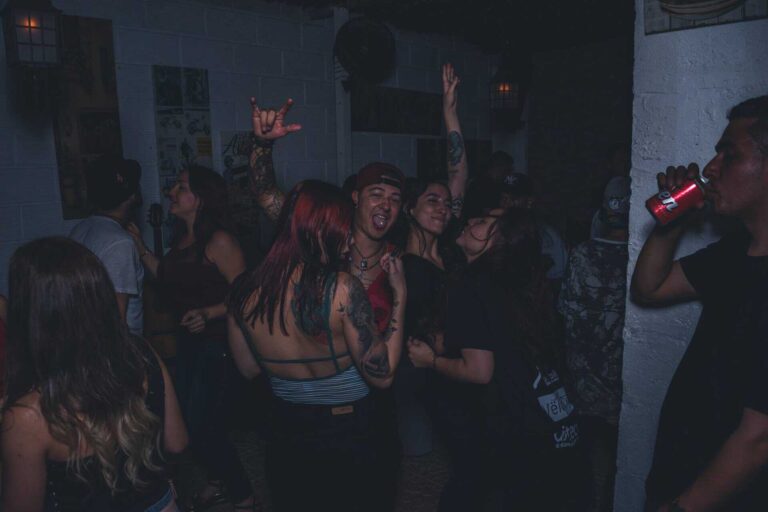 Disfraces y ambiente en evento de fiesta con jóvenes bailando y socializando en un bar con decoración moderna y música en vivo.
