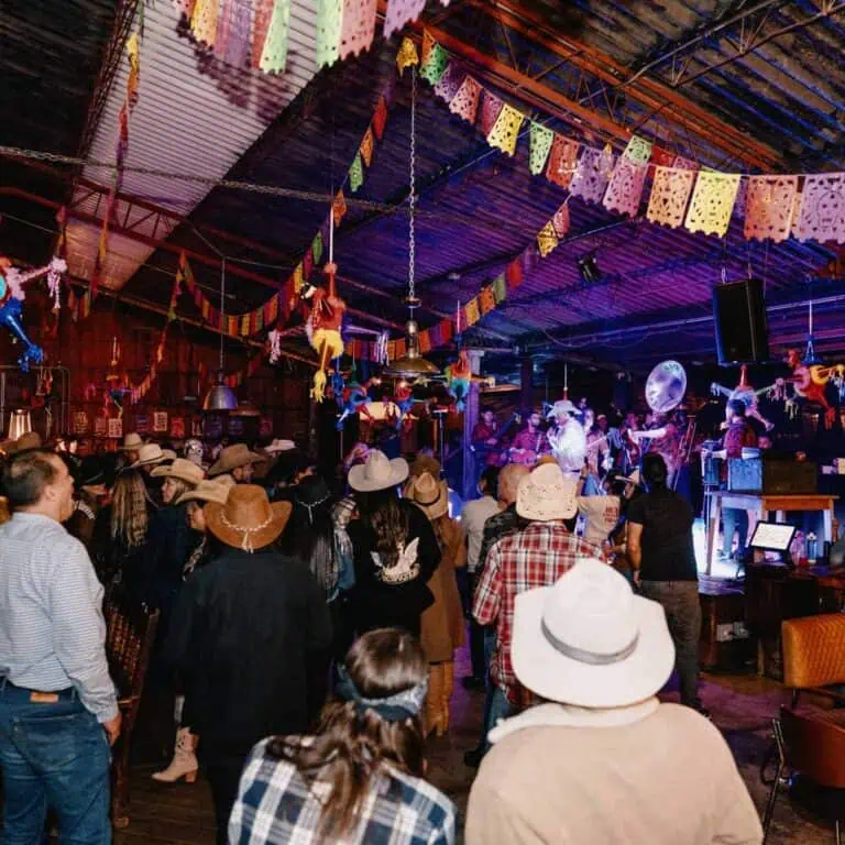 A traditional Mexican celebration takes place in a hall decorated with confetti and pennants, where a live band plays music, creating a lively, festive, and cultural atmosphere.