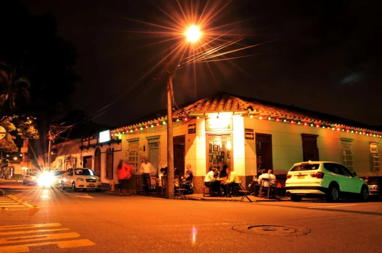 Luminoso de noche en un restaurante en la calle con decoraciones navideñas y clientes disfrutando, en un ambiente festivo y acogedor.