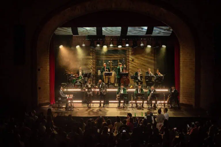 Un groupe de jazz en direct lors d'un concert dans un théâtre avec une atmosphère intime et professionnelle, un éclairage chaleureux et un public appréciant le spectacle musical.