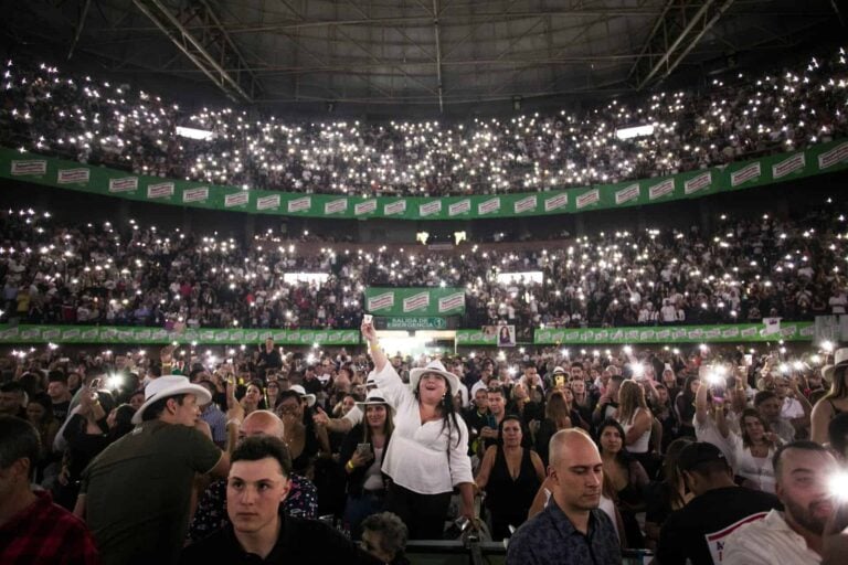 Explosión de luces y emoción en un concierto con miles de asistentes en un estadio cubierto, creando un ambiente vibrante y festivo usando luces de teléfono móvil.
