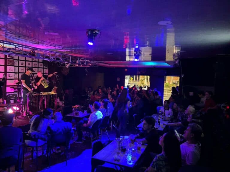 Banda en vivo actuando en un evento con público disfrutando música en un ambiente nocturno y moderno, con iluminación colorida y decoraciones que crean una experiencia vibrante y entretenida.