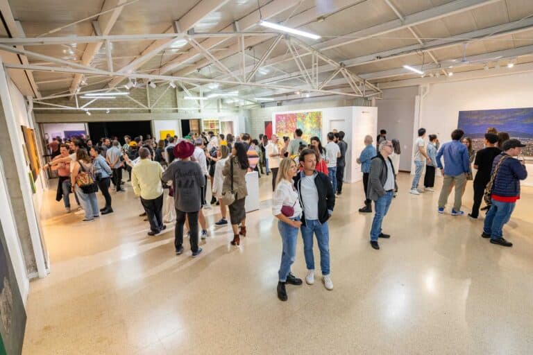 Galería de personas disfrutando y apreciando obras de arte en una exposición en un espacio cultural o museo.
