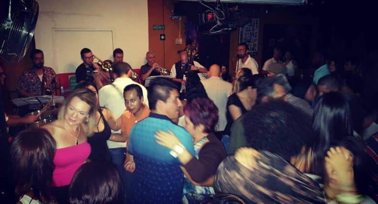 Banda musical tocando en vivo en un evento social, ambiente de fiesta y baile con asistentes disfrutando y bailando al ritmo de la música en un lugar cerrado.