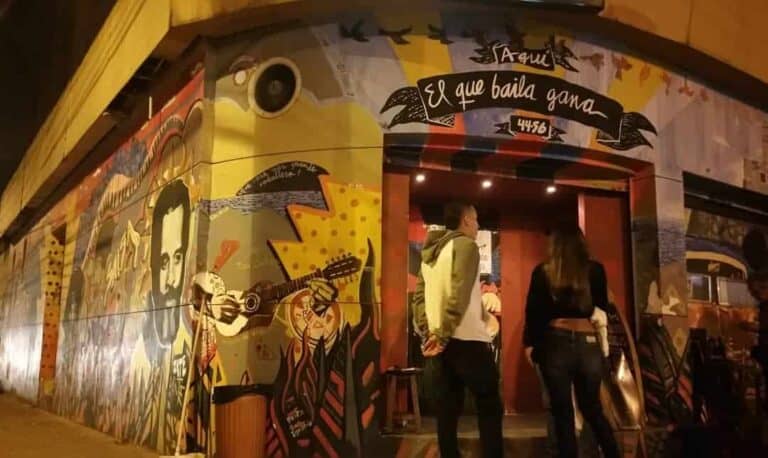 Calle de evento con mural colorido, arte urbano y personas disfrutando de la noche, entrada a evento musical en Bogotá.