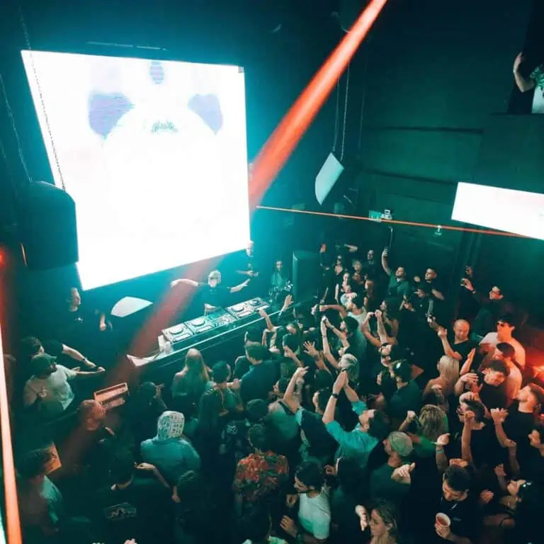Live events and entertainment in a party atmosphere featuring electronic music in a darkened room with a large screen and DJ, ideal for promoting events and festivals.