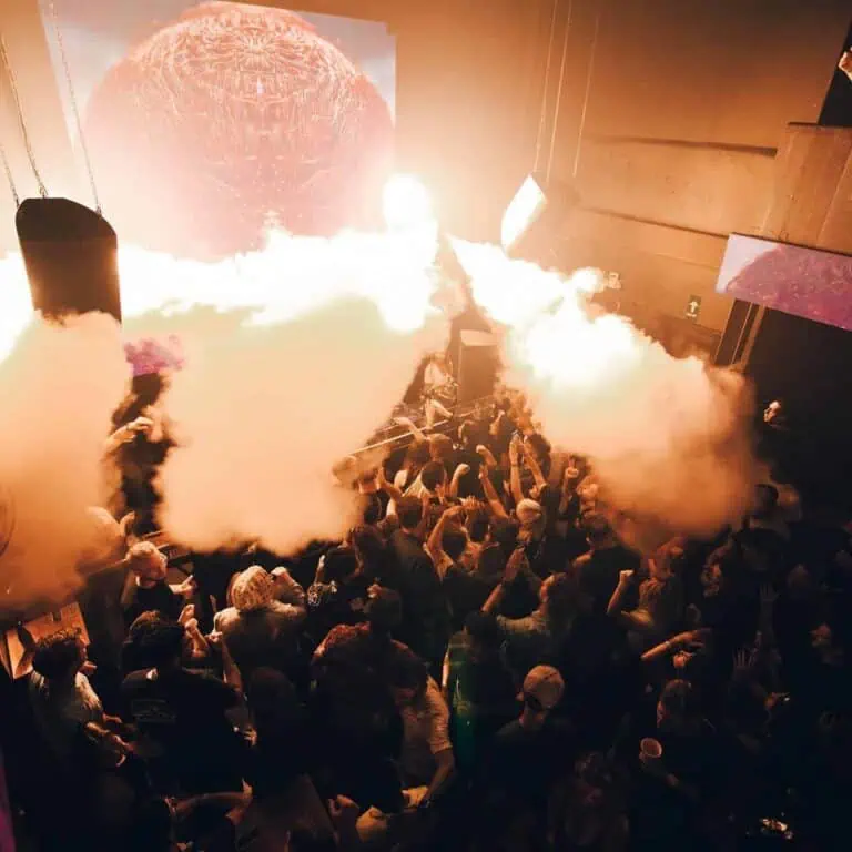 Smoke explosion and visual effects at a concert or musical event with an audience enjoying themselves on a lit stage.