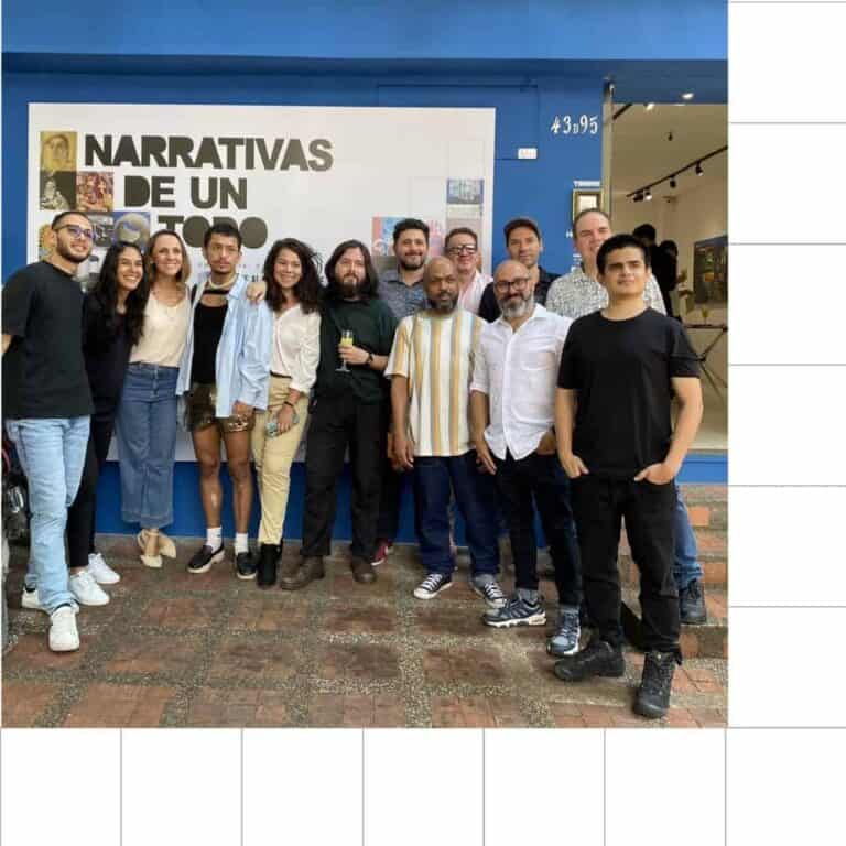 Grupo de personas sonriendo y posando en evento de narrativas en un espacio cultural, con cartel que dice "Narrativas de un todo". Ambiente social, celebración, networking y cultura en Colombia.