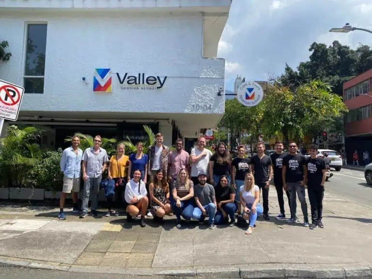 阳光明媚的城市街道上，一群人聚集在山谷西班牙语学校的入口处。