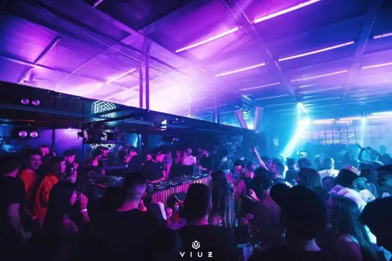 电子音乐乐队在灯光以紫色和蓝色为主的夜总会举行演唱会，观众们享受着演出，气氛充满活力和激情。