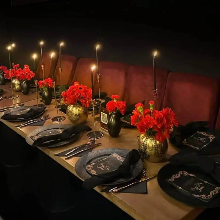 优雅的活动桌，黑色和金色花瓶中插着红色花卉，点缀着蜡烛，铺着黑色桌布，摆放着装饰盘，非常适合社交活动和主题庆祝活动。