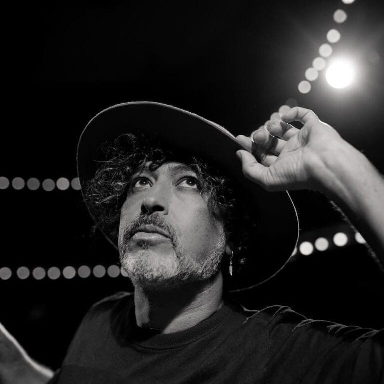 Persona sosteniendo sombrero, fotografía en blanco y negro, estilo artístico, fotografía de retrato, evento, imagen de artista en escenario, fotografía artística, para promoción de eventos y arte, fotografía en alta calidad, fotografía para marketing digital, relevancia para evento y cultura.