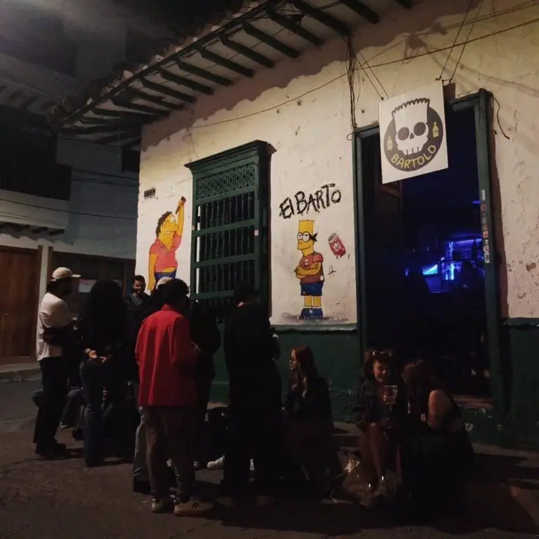 波哥大 El Barto 街区酒吧，墙上绘有辛普森一家人物壁画，夜晚氛围浓厚，人们在户外社交，风格都市而充满活力，是举办活动和社交聚会的理想场所。