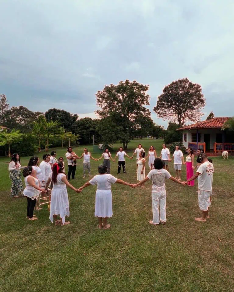 儿童和成人围成一圈，在绿树成荫、有传统房屋的户外活动中参与融合活动，以促进哥伦比亚的文化和社区活动。