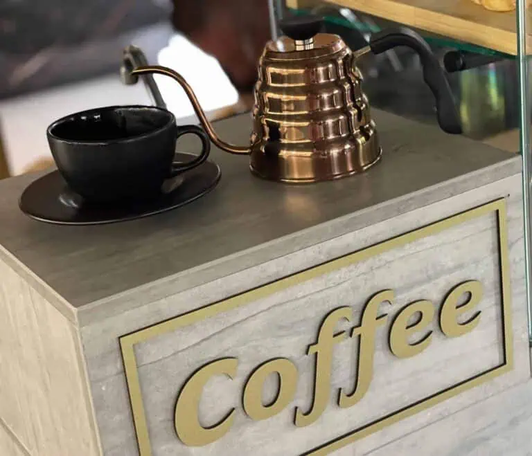 Kaffeehandwerker in einem modernen Café mit einer Kaffeemühle im Vintage-Stil und einer schwarzen Tasse auf einem Holztisch.