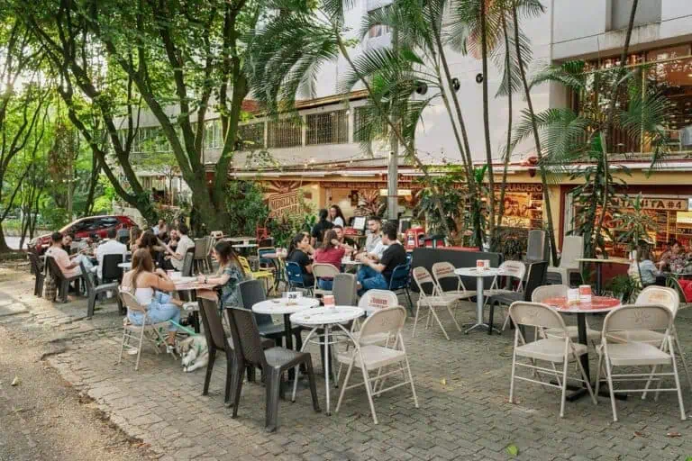 在哥伦比亚一座城市的城区，人们在被树木和植被环绕的户外餐厅露台上用餐。