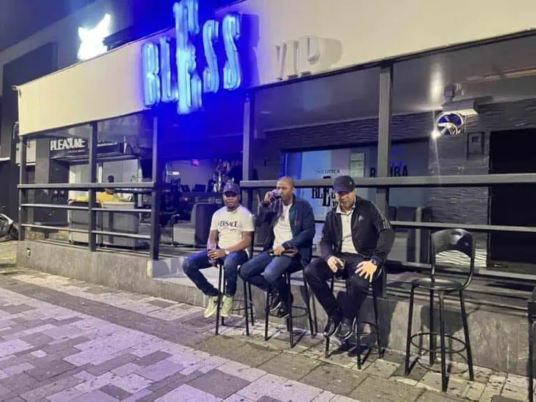 Gäste auf der Straße vor einem Restaurant mit beleuchteter Leuchtreklame, moderner Verpackung und nächtlicher Atmosphäre – urbaner und geselliger Stil.