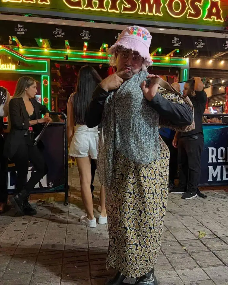 Un costume divertente e umoristico a un evento sociale, una persona con un abbigliamento appariscente a una fiera o a una festa, un'atmosfera notturna con persone che si divertono, luci al neon e un palcoscenico vivace sullo sfondo.