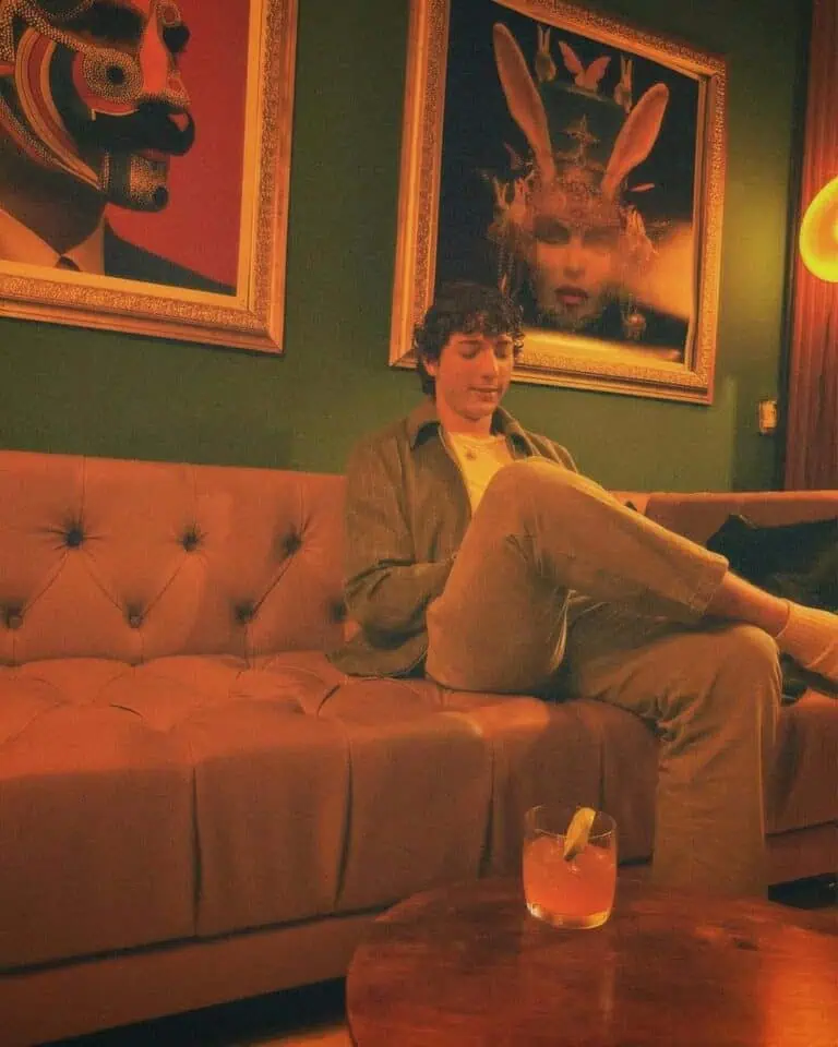 Einen Moment in elegantem Ambiente mit moderner Kunst genießen, mit einem Getränk auf dem Tisch, in einem Raum, der mit warmem Licht und Kunstwerken an den Wänden geschmückt ist.