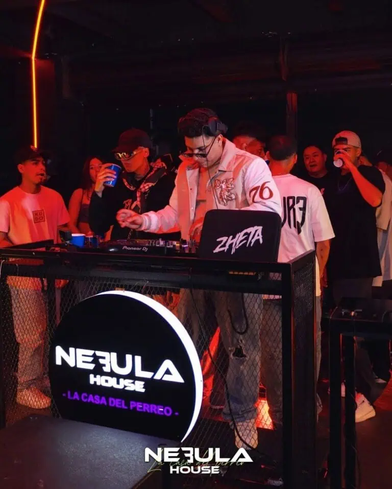 Image stamp: Neon logo on DJ table with young audience in nightclub.