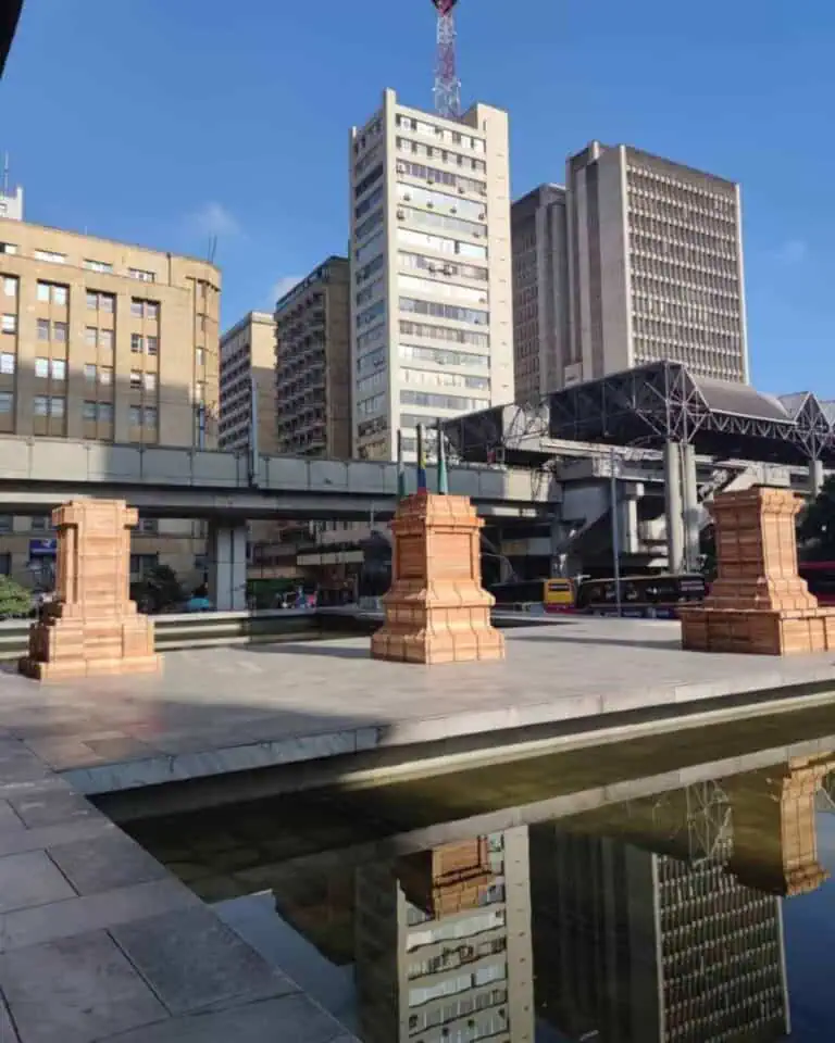 阳光灿烂的日子里，一座高耸的城市建筑倒映在水中，楼顶耸立着一座输电塔。这里是举办城市活动和庆典的理想场所，展现了现代都市建筑的风采。