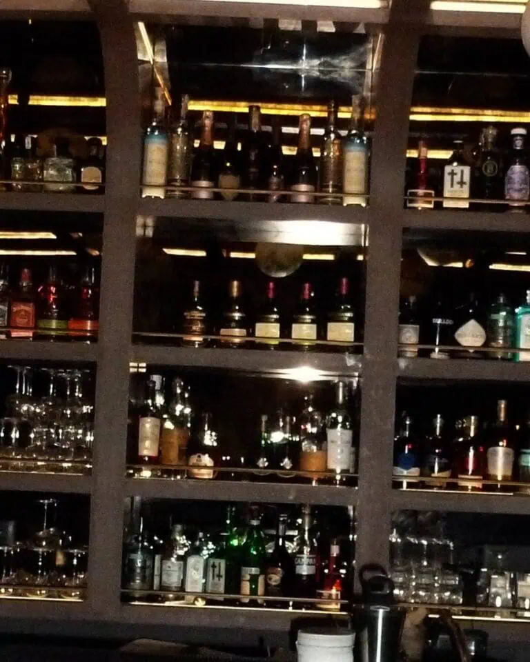 吧台架子上摆放着各种酒类饮品，营造出昏暗而优雅的氛围，是举办活动和社交聚会的理想场所，有助于组织和提供活动所需的饮品服务。