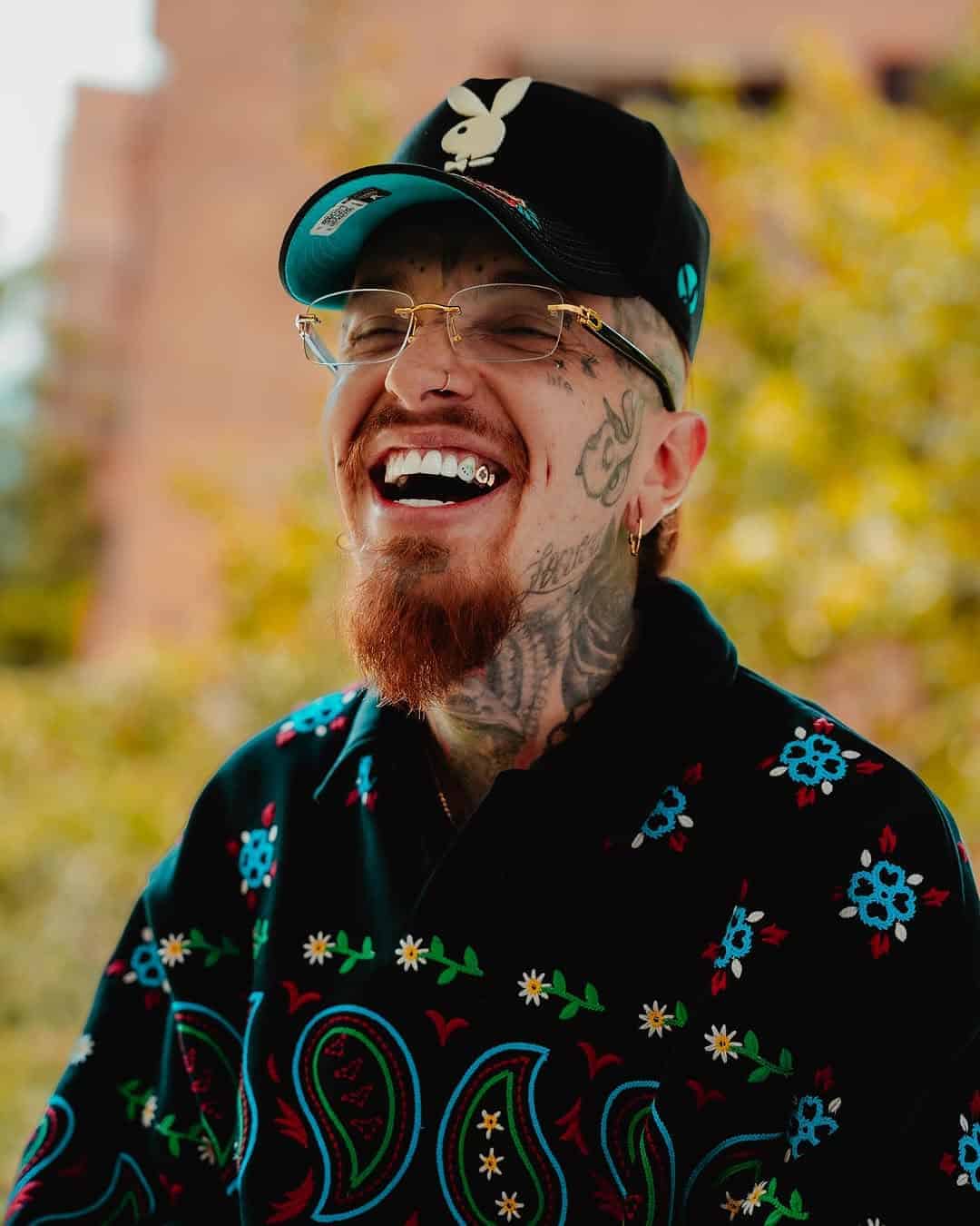 Disfrutando un momento alegre en un evento de eventos y entretenimiento en Bogotá. Persona joven con tatuajes, gafas, gorra y ropa con estampados florales, transmitiendo felicidad y diversión.