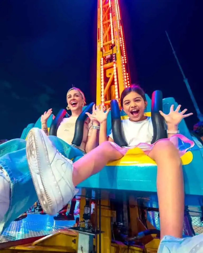 Woman and girl enjoying a roller coaster ride at an amusement park with night sky and bright lights, capturing the excitement and fun of family events and entertainment.