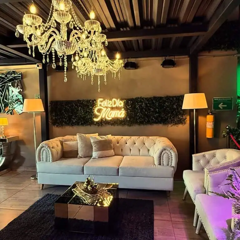 Décor événementiel élégant avec un canapé beige, des lampadaires, un lustre en cristal et une pancarte « Mom's Party », parfait pour les célébrations familiales ou romantiques.