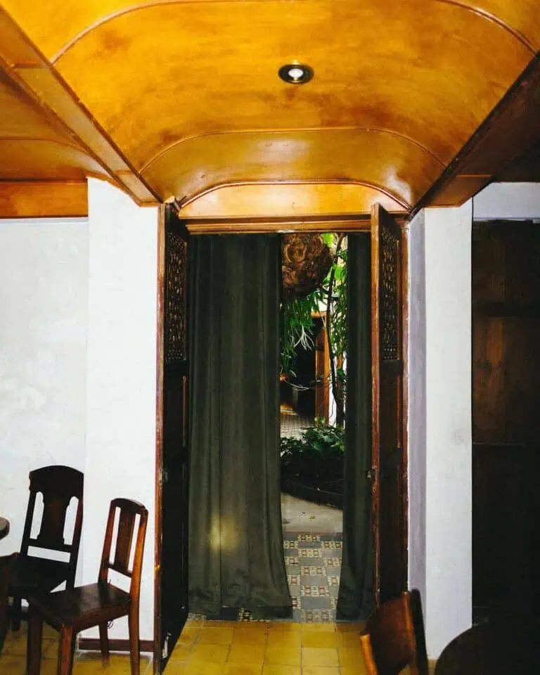 一扇挂着黑色帘子的木门通向一个绿意盎然、装饰精美的室内花园。木质细节营造出温馨宜人的氛围，活动空间内还设有用餐区。