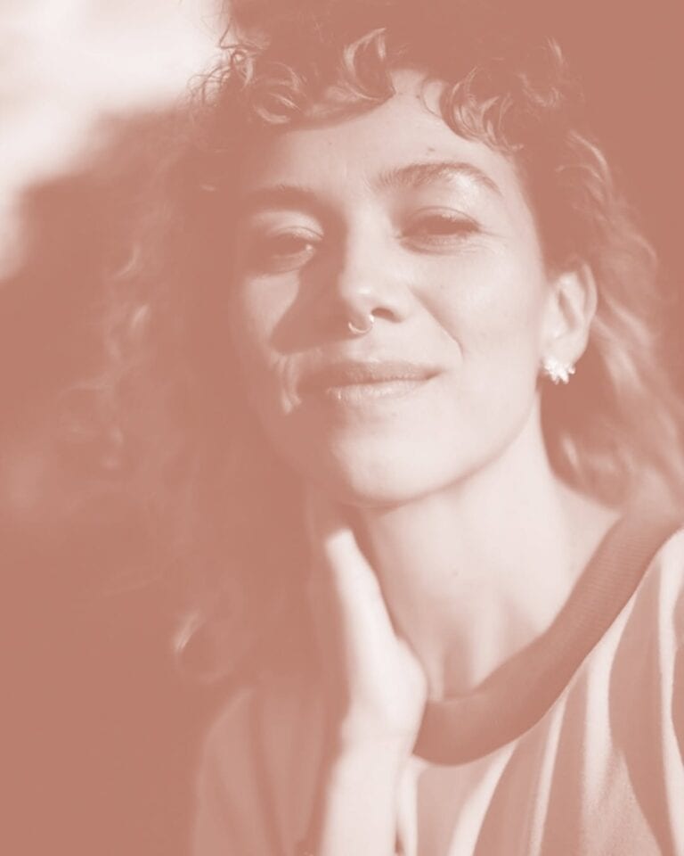 Joven mujer con estilo moderno y expresión confiada, en un retrato artístico con tonos suaves, ideal para contenido sobre eventos, moda y fotografía profesional.