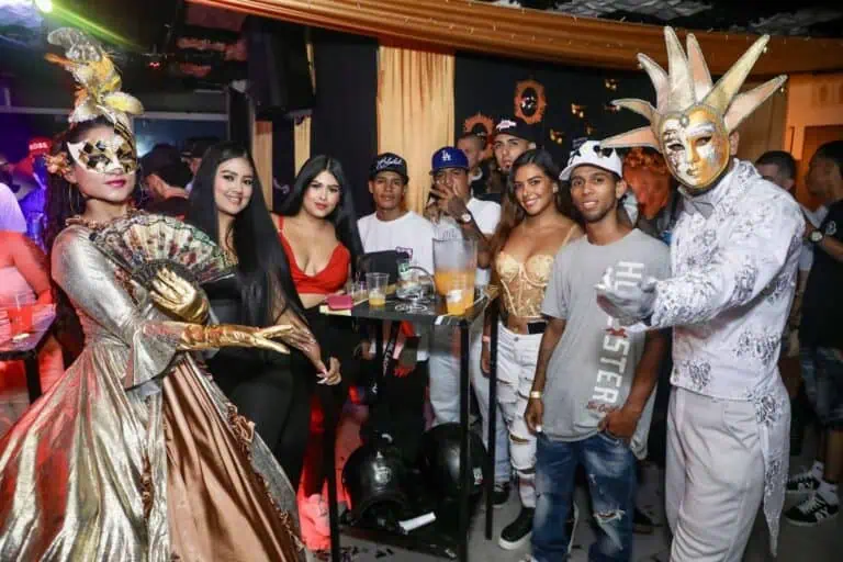 Masks and costumes at a celebratory event in Medellín. A festive atmosphere with people enjoying music and drinks in a bar or lounge.