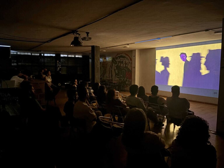 Fondo de pantalla con proyección de una animación en un evento o presentación, con espectadores atentos en un ambiente oscuro, ideal para contenidos de eventos, marketing y tecnología.