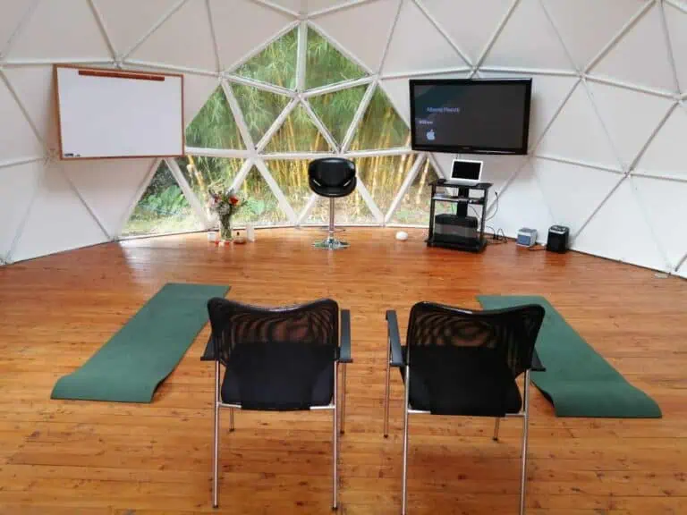 Coin yourte moderne pour événements et ateliers avec vue sur la nature, équipé d'un écran, de chaises, de tapis et d'un espace de présentation dans un environnement écologique et relaxant.