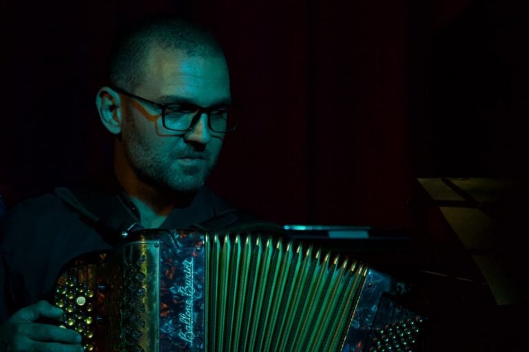 Acordeonista tocando en un evento en un ambiente oscuro con iluminación teatral.