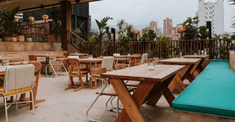 Terrasse extérieure moderne avec mobilier en bois et plantes tropicales dans un cadre urbain pour événements et réunions à Bogotá.