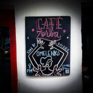 Affiche publicitaire Café Zorba avec design néon et dessin d'une femme sirotant un café, annonce d'événement à Bogotá, accès Dès 8h, avec code QR et couverture de 7 millions, dans un style informel et accrocheur.