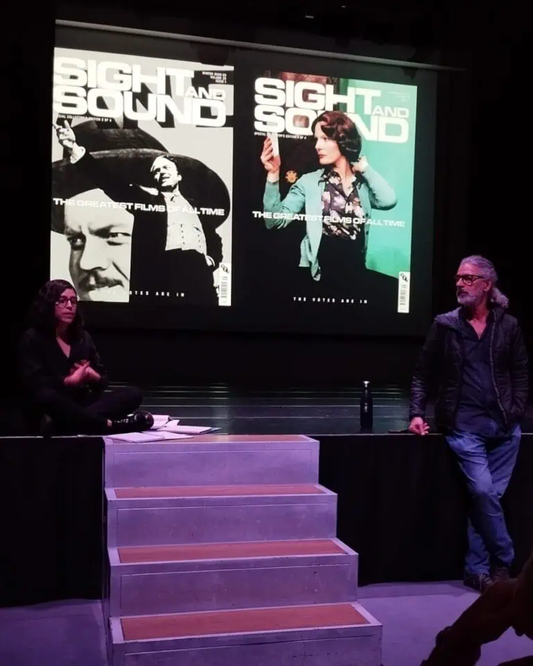 Photograph of a conference at a film and entertainment event, showing posters for the movie "Sight and Sound" on a large screen, with a woman and a man on stage.