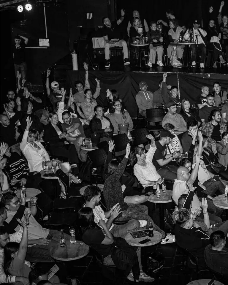 在音乐会或会议等现场娱乐活动中，观众们积极参与并举手发言。这是一张黑白照片，展现了不同背景的观众们享受活动的场景。