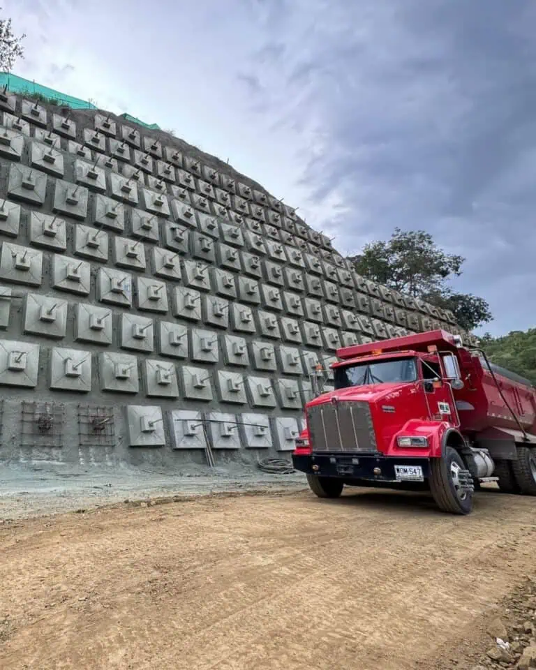 Engins de chantier et murs en gabions dans des travaux de génie civil en construction avec un camion rouge sur un site industriel en construction d'infrastructures.