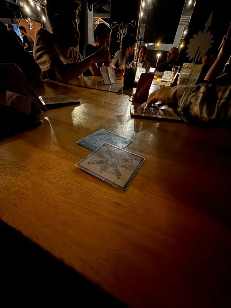 Des personnes profitant d'un événement dans un cadre sombre et moderne, avec des tables en bois, un éclairage tamisé et des boissons à disposition. Idéal pour les contenus événementiels, le networking et la restauration dans des lieux modernes.