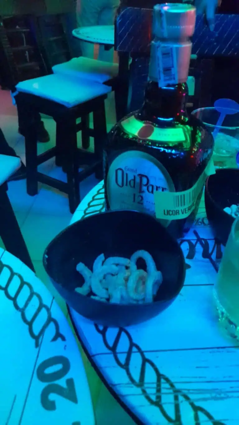 A bottle of Old Parr liquor on a table with snacks and glasses in a nighttime party atmosphere at a restaurant or bar.