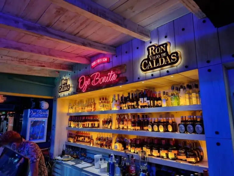 Liquor bottle on a lighted shelf, signage for "Discoteca," "Oye Bonita," and "Ron Viejo de Caldas," a bar atmosphere with modern decor and neon lights for events and nighttime entertainment.