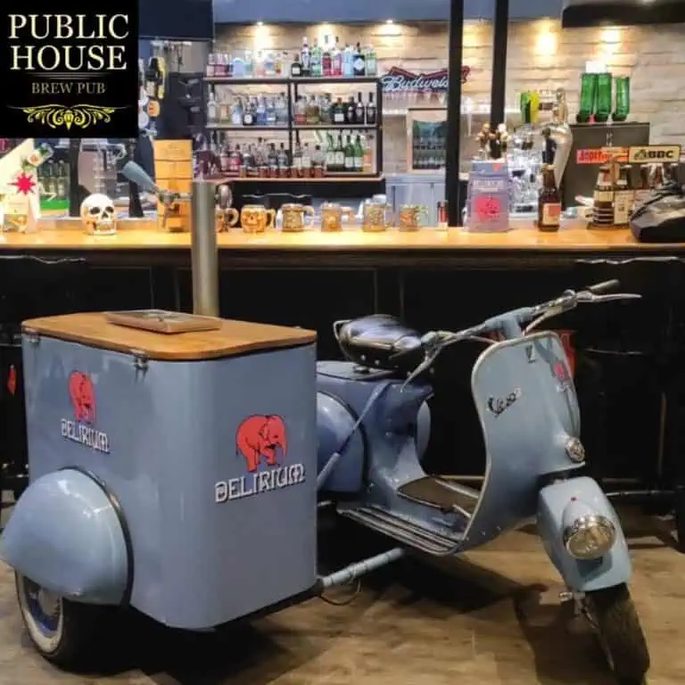 复古踏板摩托车搭配装饰冰淇淋车，摆放在啤酒鸡尾酒吧、咖啡店中，背景是摆放着饮品和酒吧用品的吧台，非常适合举办活动和品牌推广。