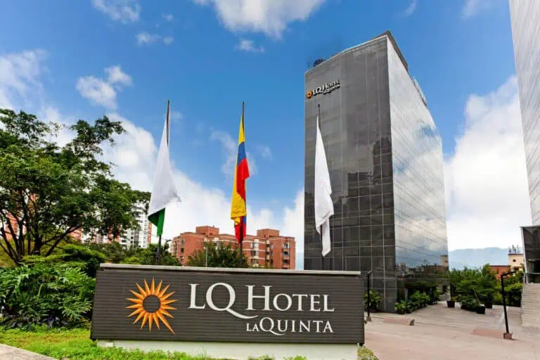 阳光明媚，蓝天白云，哥伦比亚某城市的 IQ La Quinta 酒店，在现代化的玻璃建筑中，映照着哥伦比亚国旗、厄瓜多尔国旗和另一面白旗。