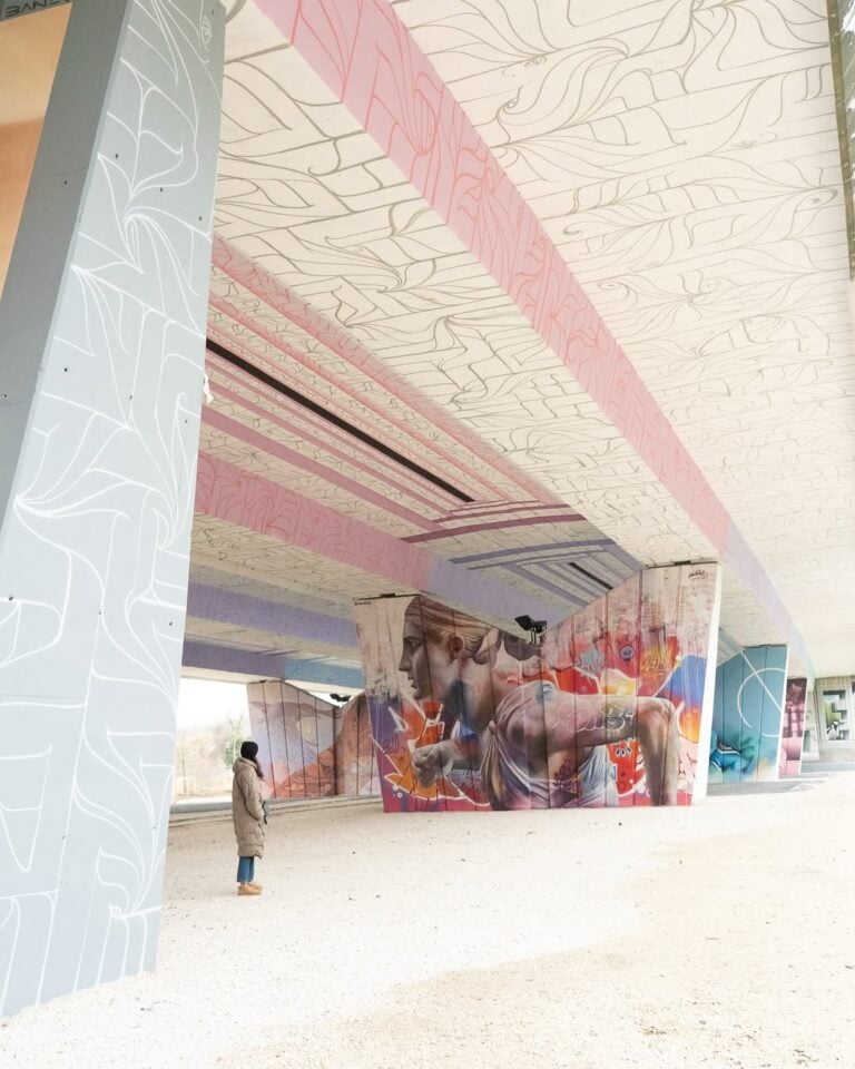 Creatividad en arte urbano en estructura moderna con mural colorido y diseños abstractos en el techo y paredes exteriores, promoviendo eventos y cultura artística.
