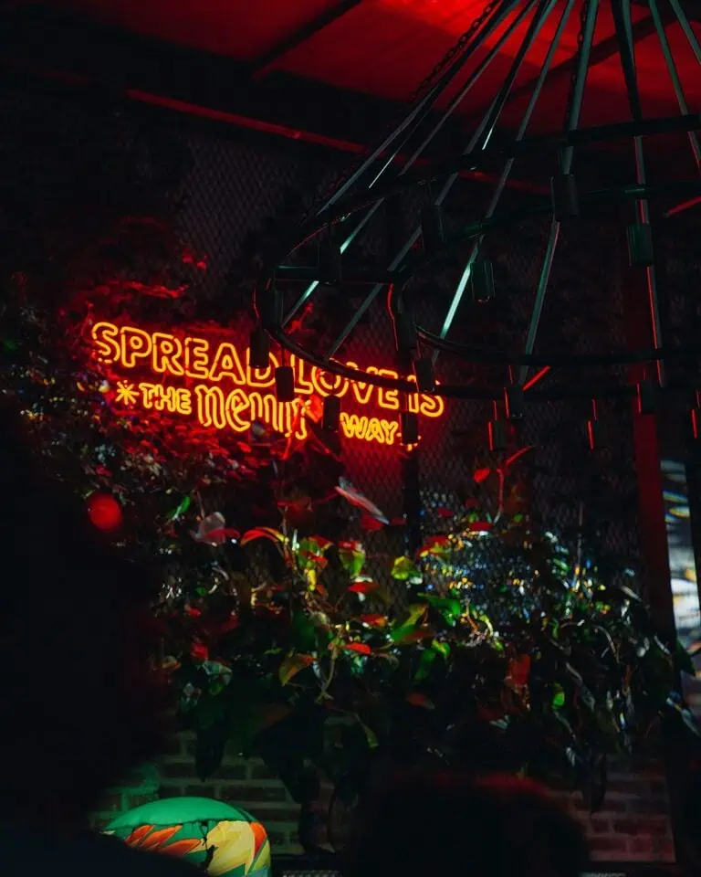 Red neon letters with the phrase "Spread love is the only way" in a dark environment, surrounded by plants and modern decor, ideal for events and entertainment in Colombia.